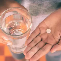 Dłoń trzyma szklankę wody i tabletkę, być może Efferalgan Codeine, by złagodzić ból.