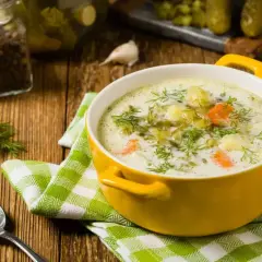Zupa ogórkowa z koperkiem i ziemniakami. W tle słoik z pieprzem, czosnek i ogórki kiszone – idealne jakie przyprawy do zupy ogórkowej.