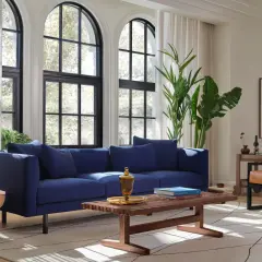 Elegancka granatowa sofa stanowi centralny punkt salonu. Aranżacje z nią tworzą przytulną atmosferę, podkreśloną przez światło wpadające przez łukowe okna.