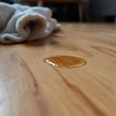 Une petite tache d'eau sur un parquet en bois. Un tissu blanc est posé à proximité, prêt à éponger.