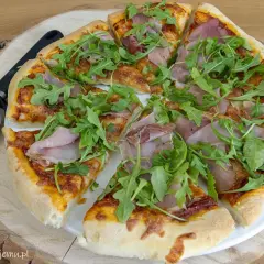 Pyszna pizza z rukolą i szynką, gotowa do podania. Idealne składniki na pizzę dla każdego smakosza.