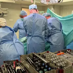 Zespół chirurgów w strojach operacyjnych podczas zabiegu, widoczne instrumenty ortopedyczne.