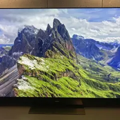 Telewizor wyświetla malowniczy krajobraz górski z zielonymi zboczami i skalistymi szczytami.