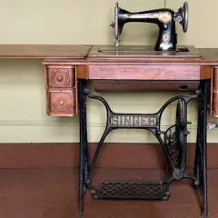 Antique Singer sewing machine on a wooden table with drawers and a treadle base.