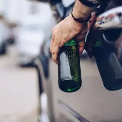 Hand hält Bierflaschen aus Autofenster. Die Frage "ab wie viel Promille ist man besoffen" wird hier thematisiert.