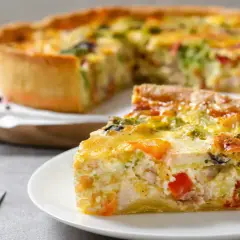 Une part de quiche savoureuse avec une pâte à tarte maison dorée, garnie de légumes et de poulet. Le reste de la tarte est flou en arrière-plan.