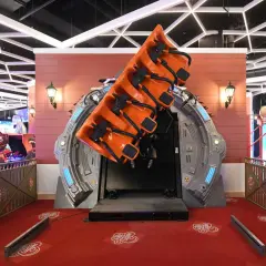 Attraction de manège orange suspendue, prête à faire décoller les visiteurs. Le sol rouge est décoré de motifs "La tête dans les nuages".