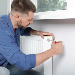 Mężczyzna reguluje zawór grzejnika, który jest do połowy zimny.