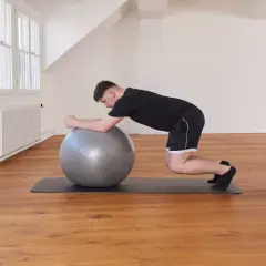 Un homme effectue un exercice de gainage avec un ballon de gym, en appui sur ses avant-bras et ses genoux.