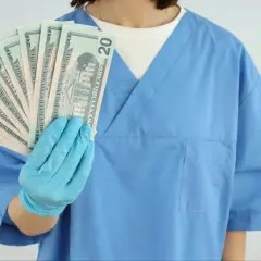 Higienistka stomatologiczna w niebieskim fartuchu pokazuje banknoty 20 dolarowe. Ile zarabia higienistka stomatologiczna?