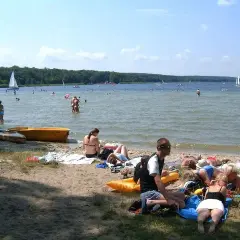 Ludzie odpoczywają na plaży, pływają i żeglują. To typowe **Boszkowo atrakcje** w słoneczny dzień.