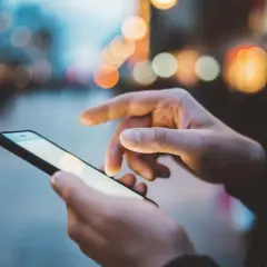 Dłonie trzymają smartfon, na ekranie którego widać rozmyte światła miasta. Szybki internet, jak APN Plus, pozwala na płynne przeglądanie.