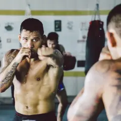 A fighter trains in a gym, punching the air. Can you go the same way twice in shadow boxing? He's focused, sweat glistening.