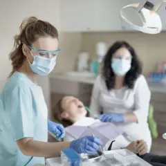 Dentystka w masce i okularach ochronnych wykonuje przegląd stomatologiczny pacjentki.