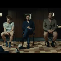 Pięciu mężczyzn siedzi na krzesłach, każdy w innym stroju. Scena z filmu "samiec alfa".