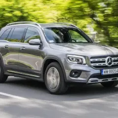 Szary Mercedes GLB 200 jedzie po drodze, otoczony zielenią drzew.