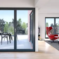 Nowoczesne okna antracytowe z widokiem na taras i ogród. W salonie czerwony fotel i kominek.