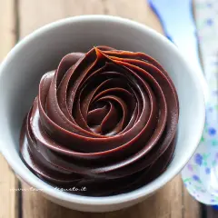 Una spirale di ganache cioccolato per copertura, lucida e invitante, in una ciotola bianca.
