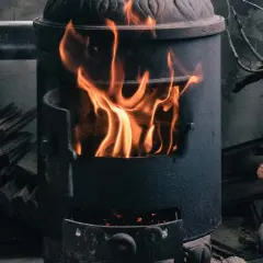 Ein Kaminofen brennt hell. Achte auf ausreichende Belüftung, um Sauerstoffmangel durch Kaminofen zu vermeiden. Holzscheite liegen daneben.