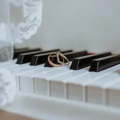 Dwa obrączki na klawiszach pianina, obok białej koronki.