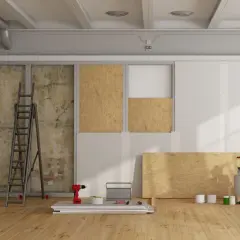 Chantier de rénovation avec panneaux de bois, échelle, outils et pots de peinture.