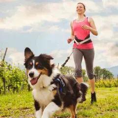 Mujer corriendo con su perro en un campo verde. La actividad física y la estimulación mental para perros son clave para su bienestar.
