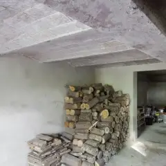 Widok stropu Kleina w przekroju, z widocznymi pustakami ceramicznymi i belkami. Obok stos drewna opałowego.