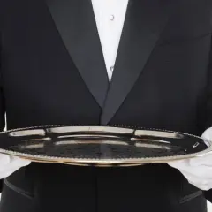 Ein Butler in schwarzem Frack mit weißer Weste und Handschuhen hält ein Silbertablett. Der Butler gehalt ist ein wichtiger Faktor für den Service.