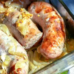 Soczysta biała kiełbasa pieczona w cebuli i musztardzie, podana w szklanym naczyniu.
