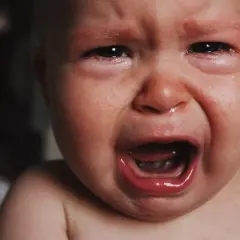 Malutkie dziecko płacze, ma zaczerwienione oczy i mokry nosek. To pewnie katar przy ząbkowaniu, który sprawia mu ból.