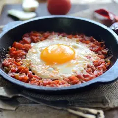 Un huevo frito sobre una cama de tomate picado en cazuelitas de aperitivo, listo para disfrutar.