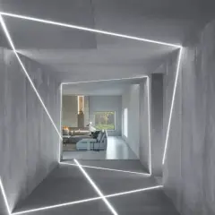 Nowoczesny korytarz z betonowymi ścianami i sufitem, ozdobiony geometrycznymi liniami światła LED. W tle widać salon z kominkiem i meblami. To inspiracja, jak zamontować oświetlenie LED w witrynie.