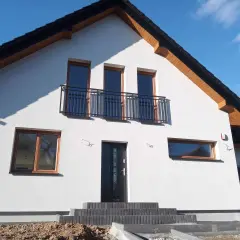 Nowy dom z białym tynkiem, antracytowym dachem i oknami w kolorze winchester.