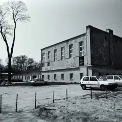 Zamek Ujazdowski w Warszawie, otoczony drzewami, z kilkoma samochodami na dziedzińcu.