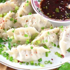 Pyszne pierożki gyoza posypane szczypiorkiem i sezamem, gotowe do zanurzenia w sosie.