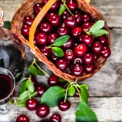 Nalewka z wiśni – przepis babci. Koszyk pełen wiśni obok kieliszka i butelki z ciemnym, aromatycznym trunkiem.