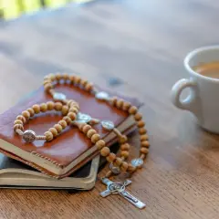 Drewniany różaniec na książkach, obok filiżanka kawy. Idealne miejsce na krótkie rozważania różańcowe.