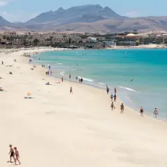 Słoneczna plaża z turkusową wodą i górami w tle. Idealne miejsce na wycieczkę na Wyspy Kanaryjskie.