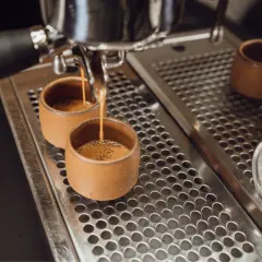 Zwei kleine Tassen werden mit Espresso gefüllt. Der Unterschied zwischen Café Crema und Kaffee Lungo wird hier deutlich: die Menge und die Crema.