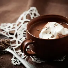 Una tazza di cioccolata calda senza cacao, con panna montata e lavanda. Un cucchiaio contiene lavanda secca.