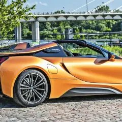 Pomarańczowy BMW i8 Roadster na bruku, pod mostem. Sprawdź aktualną bmw i8 cena.