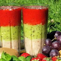 Warstwowy koktajl owocowy z truskawkami, kiwi i bananem, ozdobiony startą czekoladą, otoczony świeżymi owocami i miętą.