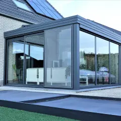 Veranda d'appartement moderne avec murs vitrés, meuble blanc à l'intérieur et une table recouverte d'une bâche.