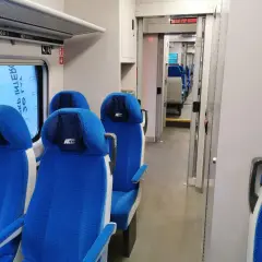 Wnętrze pociągu ed74 z niebieskimi siedzeniami i przejściem.