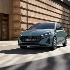 Nowoczesny Hyundai i20 w kolorze zielonym porusza się po miejskiej ulicy. To jeden z wielu stylowych modeli hyundaia.