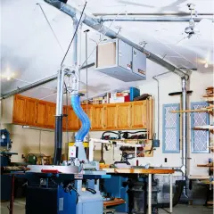 Atelier de menuiserie avec aspirateur à copeaux, tuyauterie et armoires en bois.