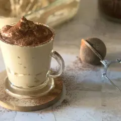 Deliziosa crema al caffè in una tazza di vetro, spolverata di cacao. Accanto, un colino per dolci e un barattolo di caffè.