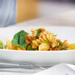 En läcker pastasallad med kyckling, gröna bönor och mynta på en vit tallrik.