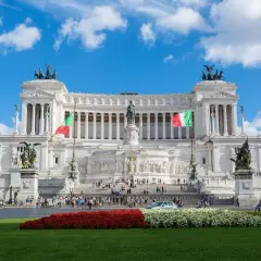Il Vittoriano, uno dei monumenti famosi di Roma, con bandiere italiane e cielo azzurro.