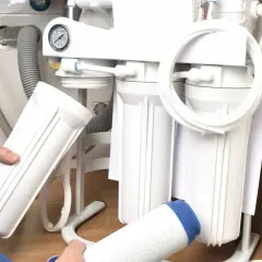 Montaż filtra do wody: ręce trzymają nowe wkłady i obudowę systemu odwróconej osmozy pod zlewem.